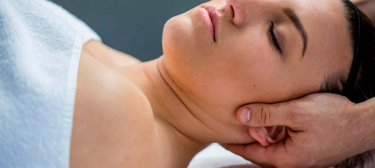 Person laying supine with massage therapist's hands on neck