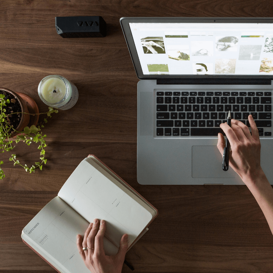 woman holding open book and typing on laptop